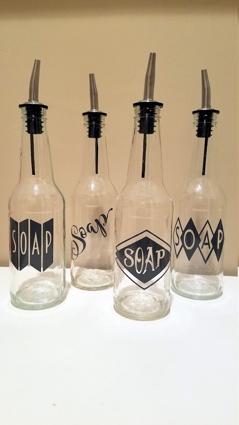 May include: Four clear glass bottles with black pump tops and black vinyl labels that say "SOAP" in different styles.