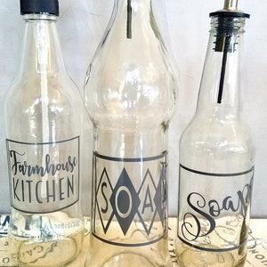 May include: Three glass bottles with black labels and pump tops. The labels read "Farmhouse Kitchen", "Soap", and "Soap".