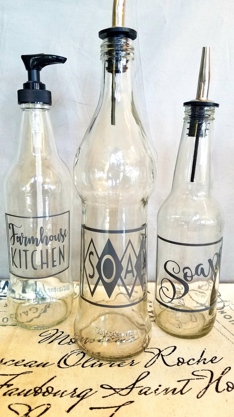 May include: Three glass bottles with black labels and pump tops. The labels read "Farmhouse Kitchen", "Soap", and "Soap".