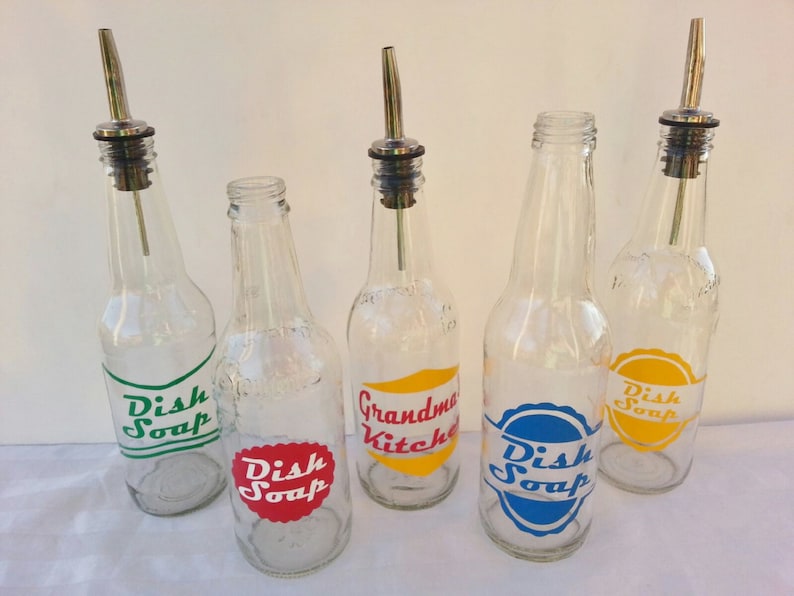 May include: Five clear glass bottles with metal pour spouts and labels. The labels are in different colors and say "Dish Soap", "Grandma's Kitchen", and "Dish Soap".