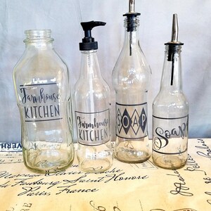 May include: Four clear glass bottles with black labels. The labels say "Farmhouse Kitchen", "Soap", and "Soap".