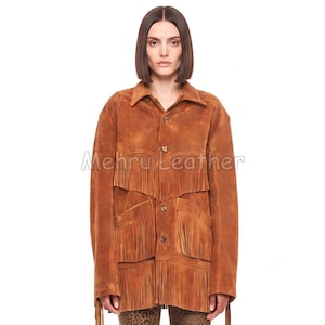 May include: A tan suede jacket featuring a pointed collar, long sleeves, and a button-down front. The garment is decorated with multiple horizontal layers of fringe across the chest and lower body. The text Mehru Leather is visible.