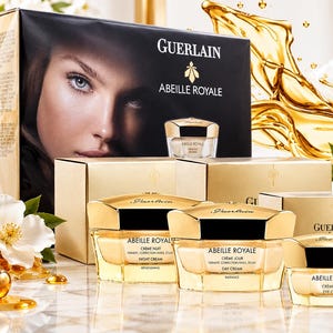 Könnte beinhalten: Ein Guerlain Abeille Royale Hautpflegeset bestehend aus drei Glasdosen mit goldenen Deckeln und passenden Schachteln. Die Produkte sind als Nachtcreme, Tagescreme und Augencreme beschriftet. Das Set enthält eine große Box mit Porträt.