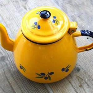 Peut inclure: Une théière en émail jaune vif avec une anse bleu foncé, un bouton de couvercle bleu foncé assorti et un motif peint de feuilles d'olivier vertes avec des olives bleu foncé réparties sur le corps et le couvercle de la théière.