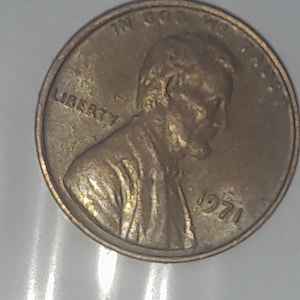 May include: A copper-colored United States one-cent coin featuring the profile of Abraham Lincoln facing right. The coin is inscribed with the word LIBERTY on the left, the phrase IN GOD WE TRUST at the top, and the year 1971 on the right side.