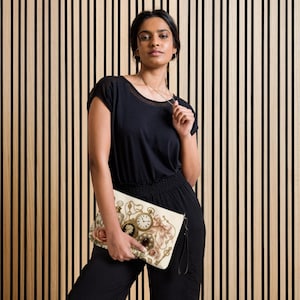 May include: A rectangular clutch bag featuring a cream-colored background with a printed design of a vintage pocket watch, a cameo brooch, a red gemstone pendant, a pink rose, a beige ribbon bow, and a gold key, finished with a black wrist strap.
