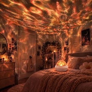 Peut inclure: Une lampe projecteur de galaxie sphérique blanche posée sur un lit projette un motif lumineux nébuleux orange et rouge tourbillonnant sur le plafond et les murs d'une chambre, créant une atmosphère dynamique et lumineuse dans toute la pièce.