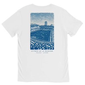 May include: A white t-shirt featuring a blue ink-style illustration on the back. The graphic depicts a crowded soccer stadium with spectators and flags. Below the stadium, the text reads ESTADIO DE LA ROSALEDA MALAGA - ESPAÑA in blue.