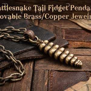 May include: A brass and copper rattlesnake tail fidget pendant on a matching metal chain. The pendant features a segmented, movable design. Text on the image reads: Rattlesnake Tail Fidget Pendant. Movable Brass/Copper Jewelry.