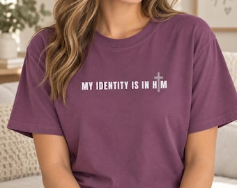 May include: A plum-colored short-sleeve t-shirt featuring the white text "MY IDENTITY IS IN HIM" printed across the chest, with a small white cross symbol replacing the letter "I" in the word "HIM" on the right side of the graphic.