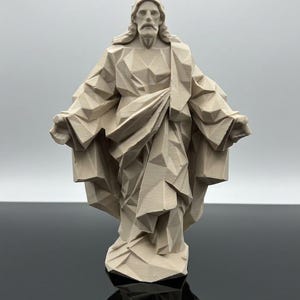 Op de afbeelding: Een beige, geometrisch low-poly beeldje van een staand figuur met lang haar en een snor, gekleed in gedrapeerde gewaden met de armen zijwaarts uitgestrekt. Het beeldhouwwerk heeft over het gehele oppervlak scherpe, hoekige facetten.