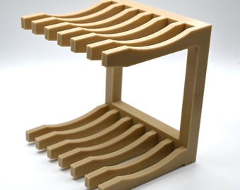 May include: A beige plastic storage rack featuring two parallel horizontal sections, each with six curved, evenly spaced slots. The structure is connected by a vertical side panel, creating an open frame design for organizing items.