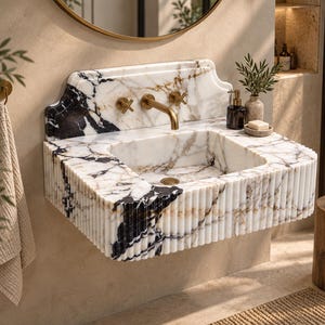 May include: A wall-mounted bathroom sink crafted from white marble with prominent black and gold veining. The basin features a fluted exterior design, a high backsplash, and a brass faucet with two cross-handle controls and a matching drain.