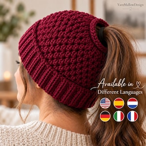 May include: A deep burgundy crochet beanie with a textured stitch pattern and a ribbed brim. The hat features a circular opening at the crown for a ponytail. Text on the image reads YarnMallowDesign, Available in Different Languages.