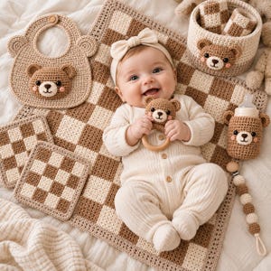 Pode incluir: Um conjunto de bebé em croché composto por uma manta aos quadrados bege e branca, um babete com motivo de urso, um chocalho com anel de madeira, um cesto de arrumação, uma capa para biberão, dois porta-copos e uma corrente de chupeta.
