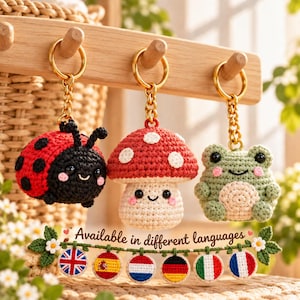 Peut inclure: Trois porte-clés en crochet représentant une coccinelle rouge et noire, un champignon rouge et blanc et une grenouille verte. Chacun possède un anneau et une chaîne en métal doré. En dessous, une bannière affiche le texte "Available in different languages" avec six petits drapeaux circulaires en crochet.
