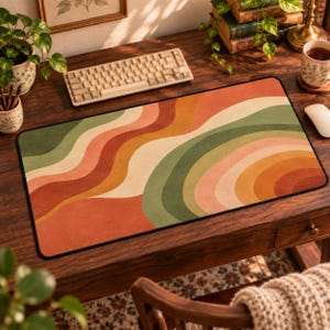 May include: A rectangular desk mat featuring a repeating pattern of wavy, curved lines in shades of terracotta, mustard yellow, cream, and sage green. The mat has a black stitched border and a smooth surface, designed to sit flat on a workspace.