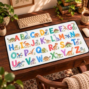 May include: A rectangular desk mat featuring a colourful watercolour alphabet from A to Z, with each letter paired with a corresponding dinosaur illustration. The design includes various species of dinosaurs in shades of green, orange, blue, and purple.