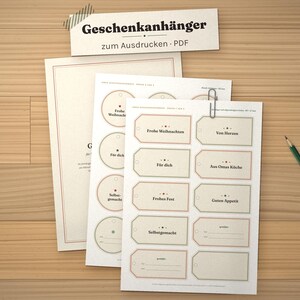 May include: A set of printable gift tags on white paper sheets featuring various rectangular and circular designs with German text including Frohe Weihnachten, F&uuml;r dich, and Selbstgemacht, accompanied by a green pencil and a metal paper clip.