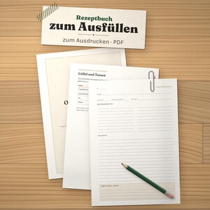 May include: A printable recipe book template featuring white sheets with black text, including the title "Rezeptbuch zum Ausf&uuml;llen" and "zum Ausdrucken &middot; PDF". The pages contain lined sections for ingredients and instructions, with a green pencil resting on top.