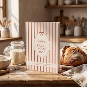 May include: A hardcover book titled Helen's BREAD BOOK with a white and brown vertical striped cover. The center features an oval frame with a bow, and the text SOURDOUGH STARTER, BREAD RECIPES & THE ART OF SCORING is printed below.