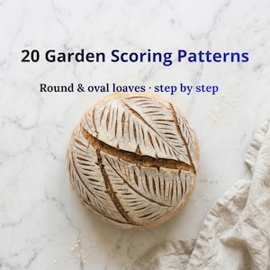 May include: A round loaf of sourdough bread featuring a decorative leaf-shaped scoring pattern on its golden-brown crust. The text 20 Garden Scoring Patterns and Round & oval loaves · step by step is displayed above the bread.