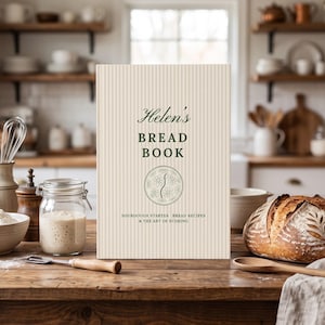 May include: A hardcover book titled Helen's BREAD BOOK with a cream-colored pinstriped cover, featuring a circular floral emblem and the text SOURDOUGH STARTER, BREAD RECIPES & THE ART OF SCORING printed in dark green on the front.