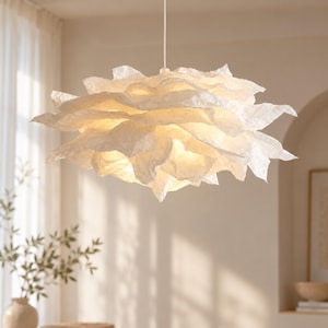 May include: A white pendant light fixture featuring a layered, crinkled paper-like shade that resembles a blooming flower. The structure is suspended by a thin white cord and emits a soft, warm glow from within its textured, overlapping petals.