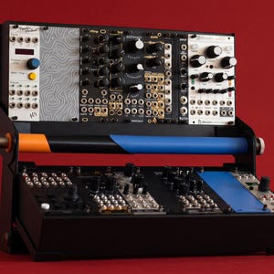 Puede incluir: Una caja de sintetizador modular con dos niveles de módulos electrónicos. La fila superior presenta un panel con patrón topográfico, mientras que la fila inferior incluye paneles negros y azules. Una barra horizontal conecta ambos niveles.