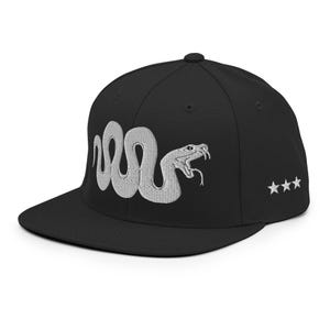 Könnte beinhalten: Eine schwarze Snapback-Kappe mit einer gestickten silbergrauen Schlange mit offenem Maul auf der Vorderseite. An der Seite der Kappe befinden sich drei kleine, weiß gestickte Sterne, die in einer horizontalen Reihe angeordnet sind.
