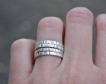 May include: A set of four silver rings stacked on a finger. The rings are textured with a hammered finish.