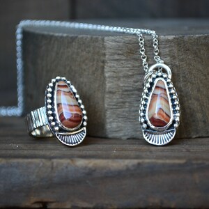 May include: A silver ring and pendant set with a teardrop-shaped red and white agate stone. The ring has a textured band and the pendant hangs from a silver chain.