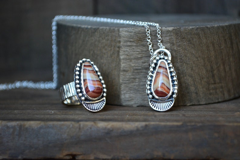 May include: A silver ring and pendant set with a teardrop-shaped red and white agate stone. The ring has a textured band and the pendant hangs from a silver chain.