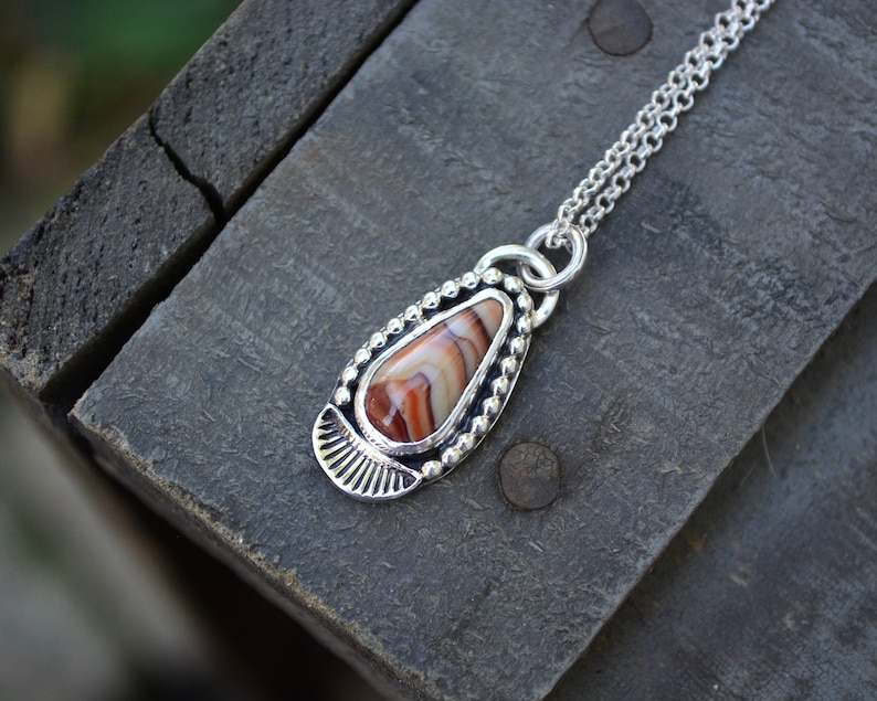 May include: A silver necklace with a teardrop-shaped pendant featuring a red, white, and brown agate stone.