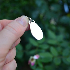 May include: A silver charm in the shape of an oval, with a smooth, polished surface. The charm is hanging from a silver loop.