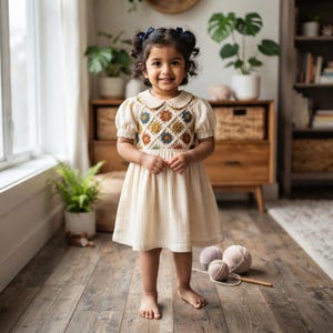 May include: A cream-colored dress featuring short puff sleeves, a rounded collar, and a bodice decorated with a diamond-patterned crochet overlay. The crochet section includes small, multi-colored floral motifs in shades of blue, yellow, and brown.