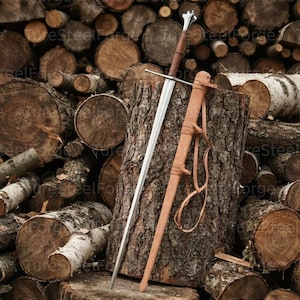 May include: A longsword with a double-edged steel blade, a brown leather-wrapped grip, and a silver-toned pommel. The sword is accompanied by a matching brown leather scabbard featuring integrated leather straps for carrying or attachment.