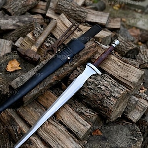 Puede incluir: Una espada de doble filo con hoja de acero pulido, empuñadura de madera oscura y pomo plateado. Junto a ella hay una vaina de cuero negro con remaches y cordones metálicos, además de un martillo oxidado y unas tenazas de metal.