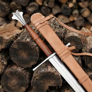 Puede incluir: Una maza con cabeza de acero pulido con bridas y mango de madera marr&oacute;n, acompa&ntilde;ada de una funda de cuero color canela con bordes cosidos y correas ajustables. La cabeza de metal tiene una forma distintiva de m&uacute;ltiples puntas.