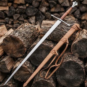 Puede incluir: Una espada larga de acero con hoja de doble filo, guarda recta y empu&ntilde;adura forrada en cuero marr&oacute;n que termina en un pomo met&aacute;lico. Junto a la espada hay una vaina de cuero color canela a juego con correas y hebillas integradas.