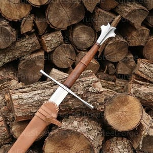 Puede incluir: Una espada larga con hoja de metal plateado, guarda recta y empu&ntilde;adura envuelta en cuero marr&oacute;n. El pomo presenta un dise&ntilde;o estriado de varios l&oacute;bulos. La parte inferior de la hoja est&aacute; encajada en una vaina de cuero color canela con costuras.