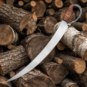 May include: A curved steel blade with a pointed tip and a metallic finish. The handle features a dark brown leather wrap and a curved metal guard that loops back towards the blade. The metal surface shows a subtle texture and a sharp, tapered edge.