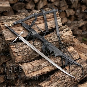 Puede incluir: Una espada larga de acero con punta afilada, una guarda de cruz plateada y un mango negro. Se acompaña de una vaina de cuero negro con recortes decorativos y un arnés de cuero negro a juego con una hebilla de metal para su transporte.