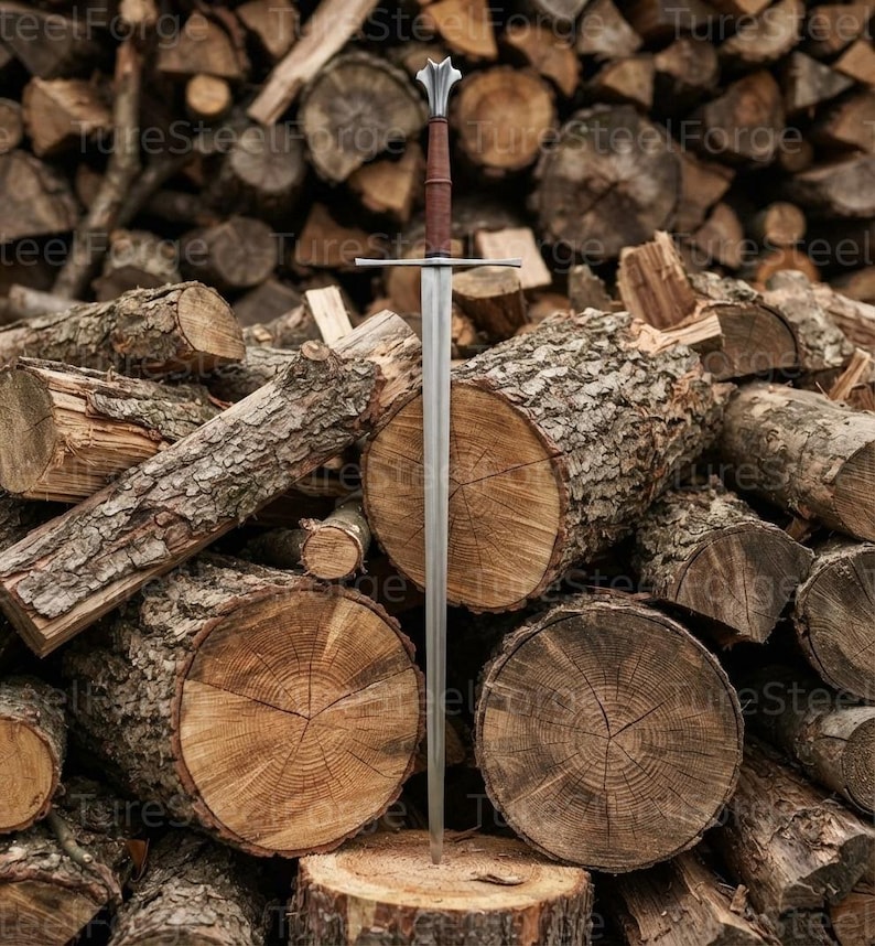 Puede incluir: Una espada larga con hoja de acero de doble filo, una guarda recta y una empu&ntilde;adura envuelta en cuero marr&oacute;n. El pomo tiene forma de flor de lis estilizada. La espada se encuentra en posici&oacute;n vertical frente a una pila de troncos.