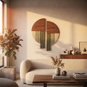 May include: A two-piece wall art set featuring semi-circular wooden panels with a natural grain finish. Each panel is adorned with long, hanging fiber fringe in varying shades of cream, light green, and dark olive, creating a layered texture.