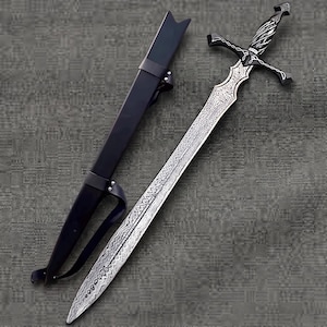May include: A silver-toned sword with a complex, etched pattern on the blade and a dark, twisted handle featuring silver crossguard detailing. The sword is accompanied by a long, black scabbard with a matching black strap and metal rivets.