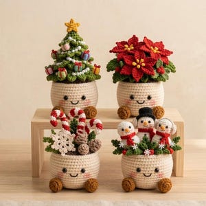 Op de afbeelding: Vier gehaakte kerstdecoraties in crèmekleurige potjes met lachende gezichtjes. De set bevat een groene kerstboom met versiering, een rode kerstster, zuurstokken met een sneeuwvlok en drie kleine sneeuwpoppen met groen blad.