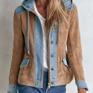 May include: A tan suede jacket featuring light blue denim accents on the hood, front placket, cuffs, and pocket flaps. The jacket includes a front zip closure, metal buttons, and a drawstring hood with matching light blue denim cords.