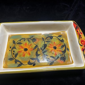 May include: A rectangular ceramic serving tray with a cream-colored interior and a yellow-green rim. The center features a hand-painted design of two orange and yellow sunflowers surrounded by dark green leafy vines on a golden yellow background.