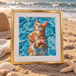 May include: A square cross-stitch embroidery featuring an orange tabby cat floating in bright blue water, enclosed in a thin gold-coloured frame with a white mat border. The artwork displays a pixelated texture created by individual stitches.